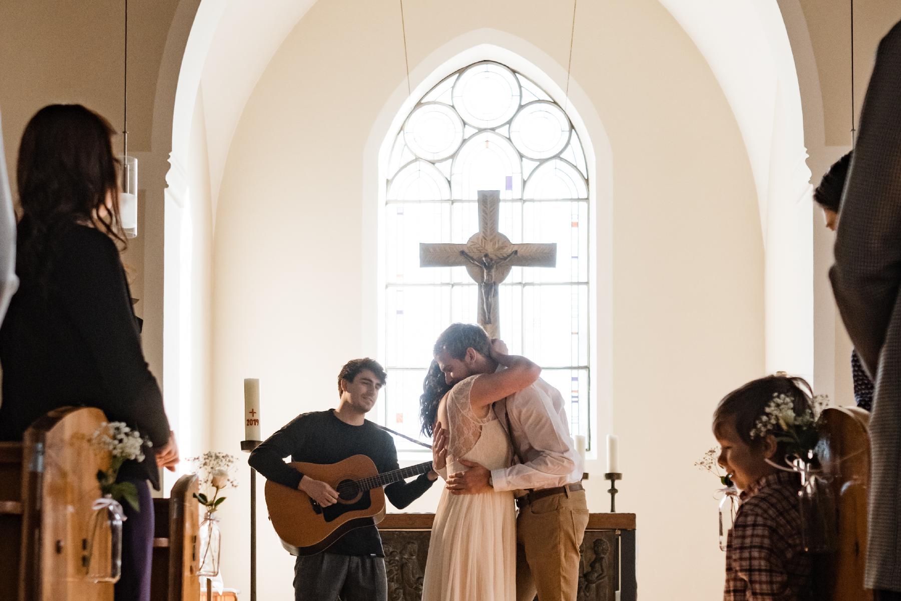 Ehepaar umarmt sich vor Altar mit Musiker im Hintergrund 