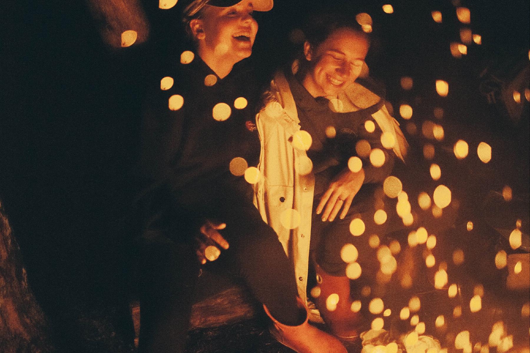 Zwei Frauen sitzen am Lagerfeuer und lachen