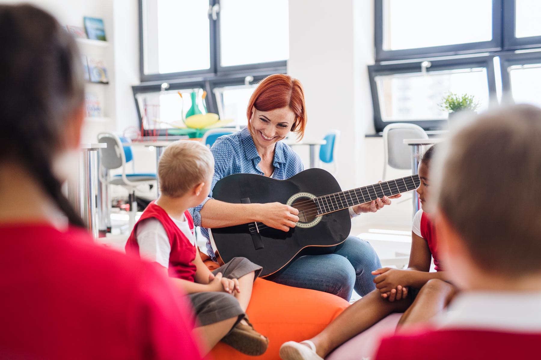 a group of small school kids and teacher with guitar